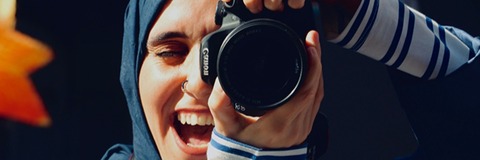 Frau mit Kopftuch die gerade fotografiert und dabei lächelt