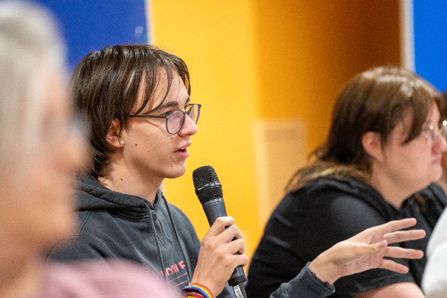 Sitzende Personen, eine Person hält ein Mikrofon und spricht.