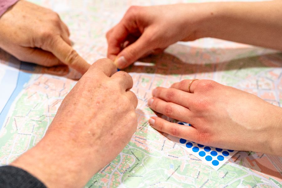Hände über dem Linzer Stadtplan, die auf einen Ort zeigen und ihn mit einem blauen Punkt bekleben.