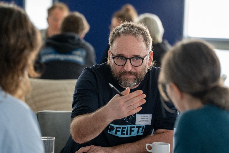 An einem Tisch sitzende Personen, eine Person spricht und gestikuliert.