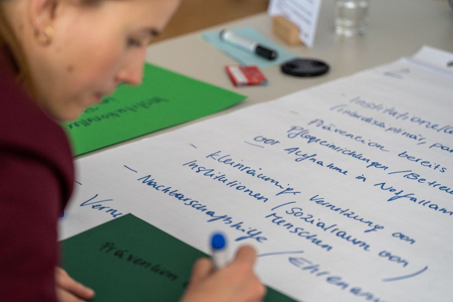 Eine Person schreibt Notizen mit blauem Marker auf ein grünes Blatt Papier.